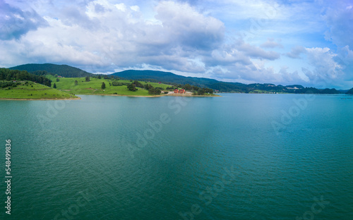 Hotels on shores of lake with reflection of mountains Rhodope against cloudy sky. Panorama, top view