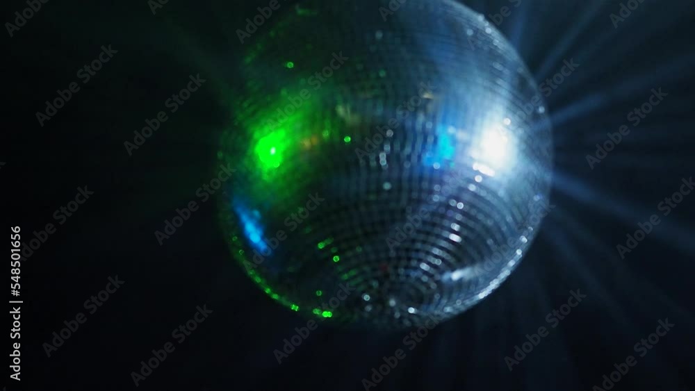 A shining disco ball is spinning under the ceiling, beams of light and a laser projector, light music at a party. Festive background A shining disco ball is spinning under the ceiling, beams of light and a laser projector, light music at a party. Festive background
