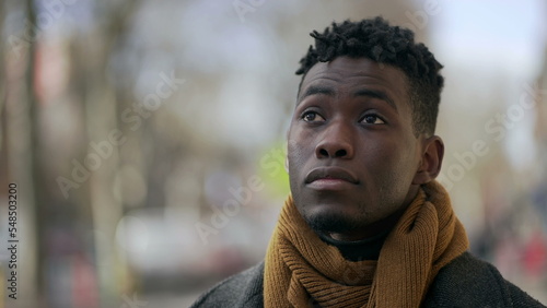 Thoughtful black man standing outside close-up face portrait in city tracking shot during winter