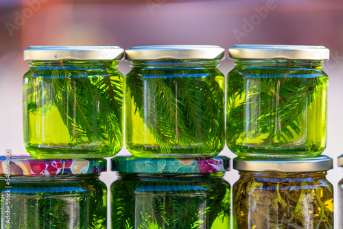 Jars of honey with green spruce needles and forest herbs stand on a street market in a row. Close up glass jars with flavoured honey. Ukraine