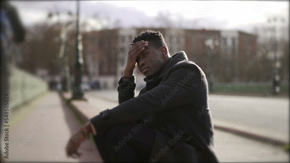 Worried black man sitting on floor in street having problems rubbing face with hand Worried black man sitting on floor in street having problems rubbing face with hand