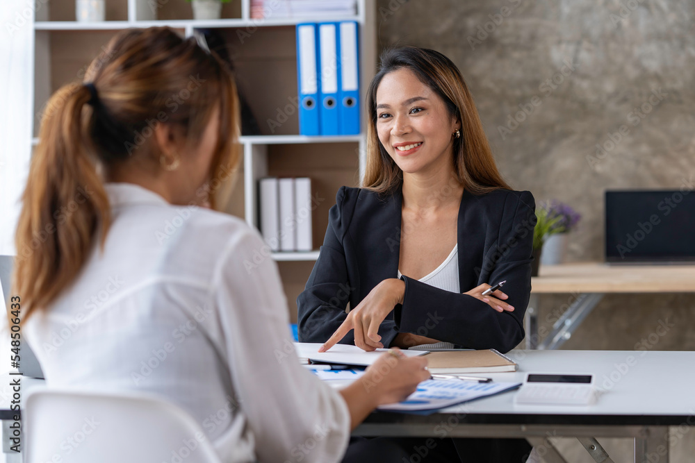 Two young businesswomen pointing to plans, statistics, and data graphs and explaining the conditions of their partnership, happily acknowledging their turnover and income during negotiations. Two young businesswomen pointing to plans, statistics, and data graphs and explaining the conditions of their partnership, happily acknowledging their turnover and income during negotiations.