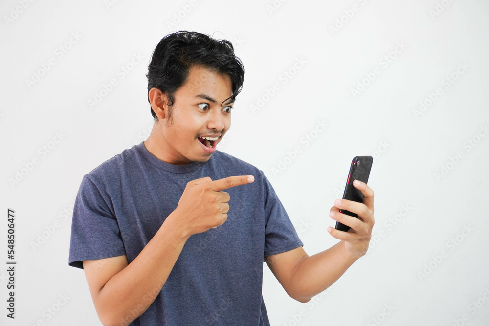 Asian man showing surprised facial expression while reading message while pointing at his phone with his finger Asian man showing surprised facial expression while reading message while pointing at his phone with his finger