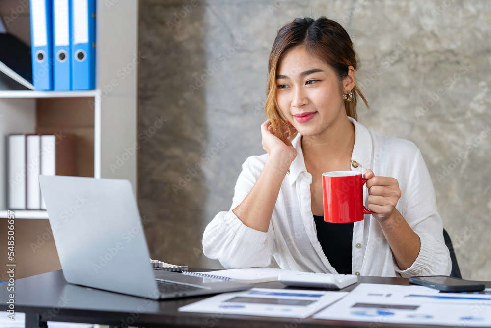 Attractive businesswoman holding cup of hot drink and looking away with smile while sitting in office. Attractive businesswoman holding cup of hot drink and looking away with smile while sitting in office.