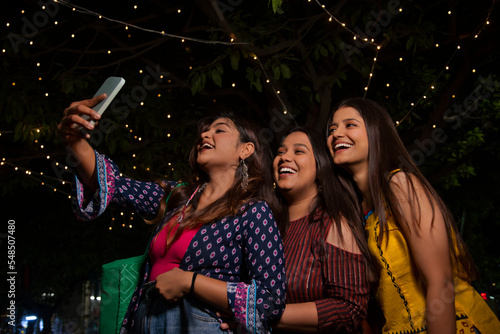 Women taking selfie together on city street at night photo