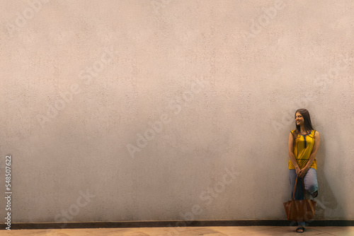 Long distance shot of an Indian woman with bag standing against wall photo