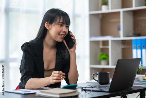 Business freelance asian woman talking on phone and working on laptop computer managing her business in workplace, doing business plan on calculator accounting financial report.