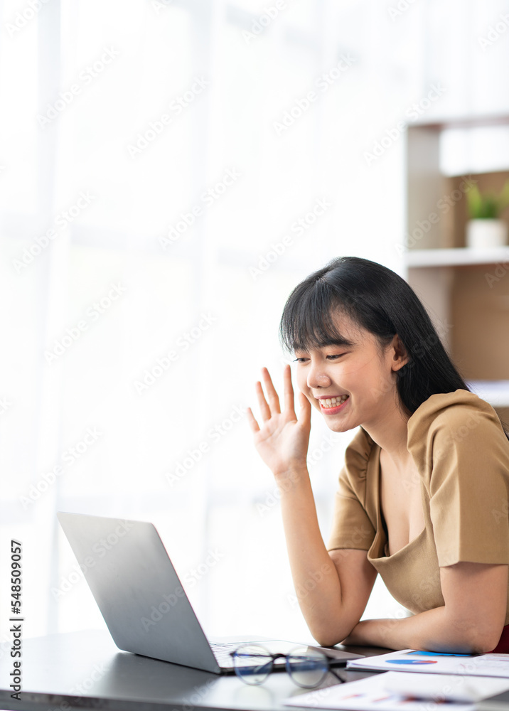 happy asian businesswoman waving hand while sitting on couch and having video chat on laptop happy asian businesswoman waving hand while sitting on couch and having video chat on laptop