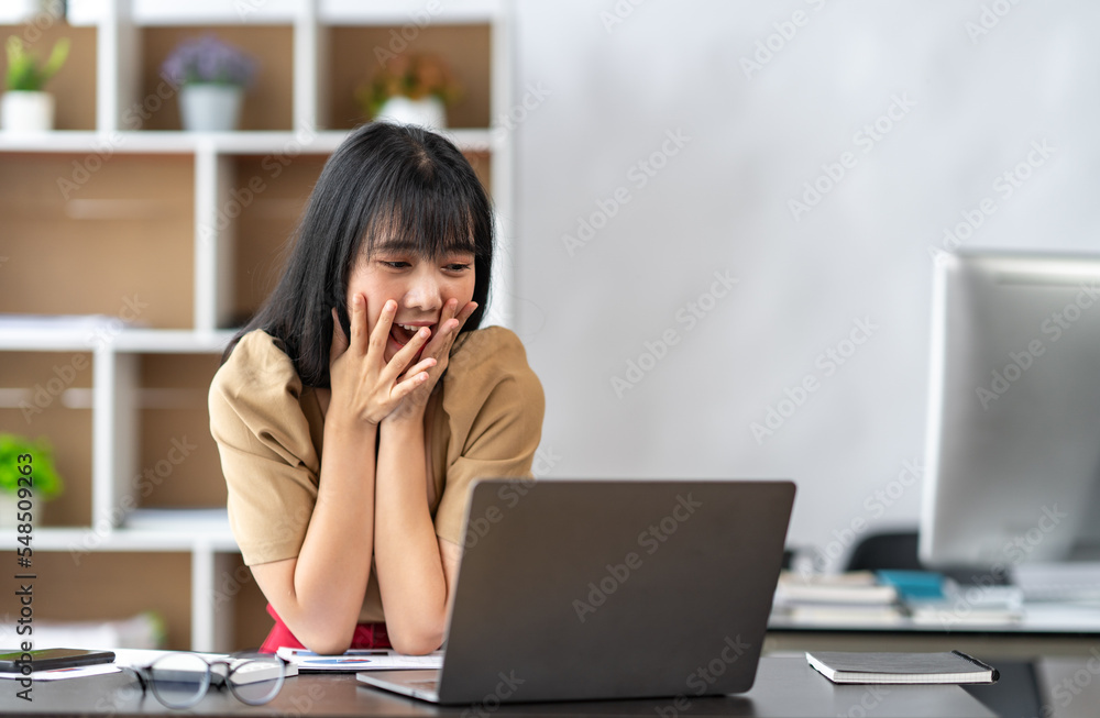 portrait Asian young woman looking at laptop screen laughing with good news or discount voucher for shopping online at home.Happy and cheerful woman looking on laptop app read message feels excited portrait Asian young woman looking at laptop screen laughing with good news or discount voucher for shopping online at home.Happy and cheerful woman looking on laptop app read message feels excited