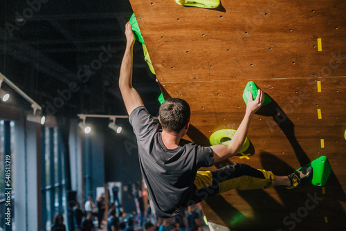 A young, strong guy in a gray T-shirt and blue shorts of athletic build climbs a bouldering in a climbing center at a competition photo