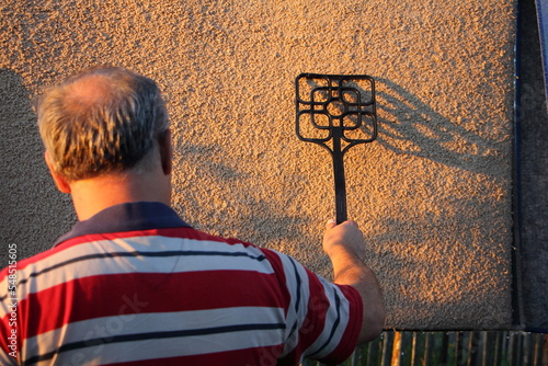 Balding man cleans a carpet outdoors at summer evening in sunset.