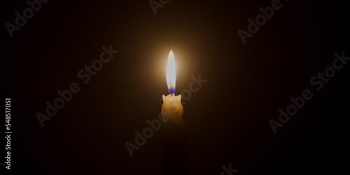 A single burning candle flame or light glowing on a spiral white candle on black or dark background on table in church for Christmas, funeral or memorial service