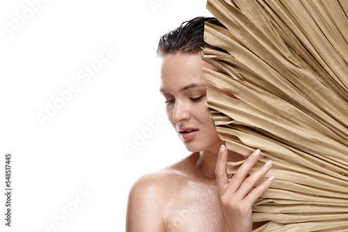 Middle aged naked woman with healthy wet skin and hair holds dry palm leave on white isolated background. Skin care beauty concept.