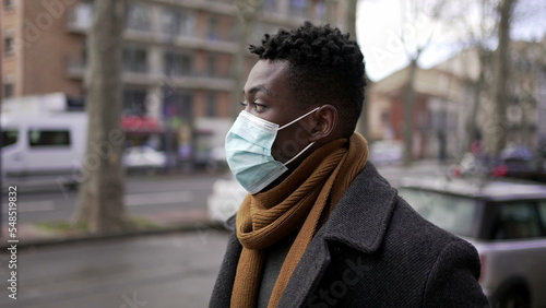Young black man wearing covid-19 face mask walking in city downtown during pandemic, tracking shot