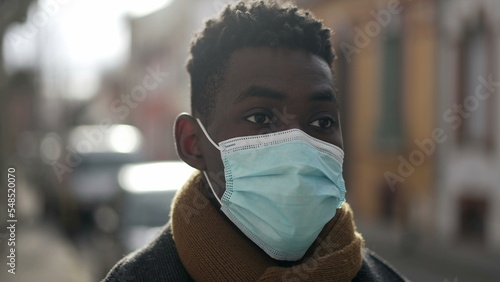 Young black man wearing covid-19 face mask standing outside in sunlight looking at camera