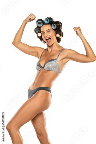 Happy woman in underwear with hair curlers on her head showing biceps and perfect body on a white background