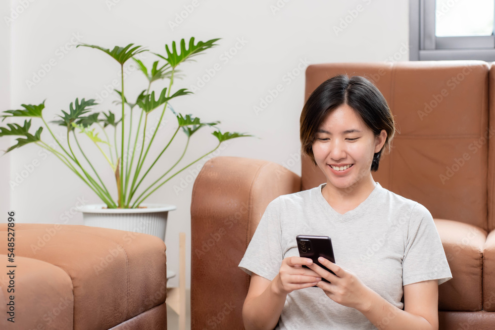Asian woman sitting on mobile phone and smiling happily at home Asian woman sitting on mobile phone and smiling happily at home
