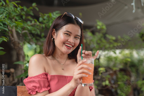 A beautiful Asian female holds the straw of her cold refreshment as she spends her leisure time by chilling in an outdoor coffee shop.