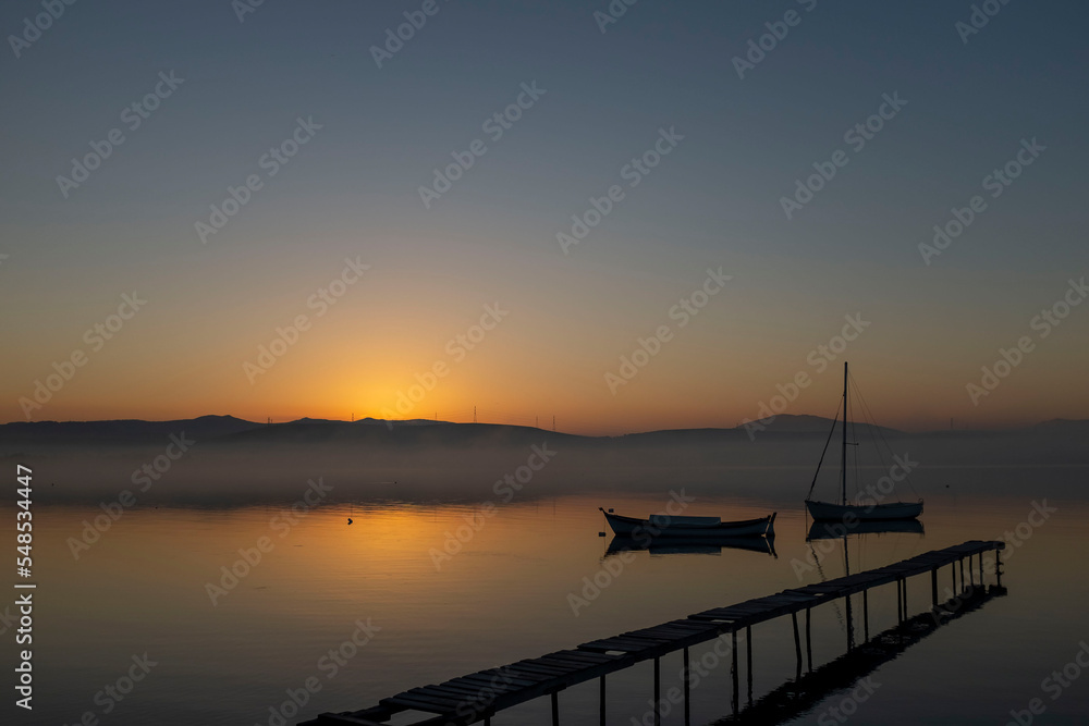 View of boats and pier on sunset sunrise or midday with reflection on water and sun light with cloudy sky