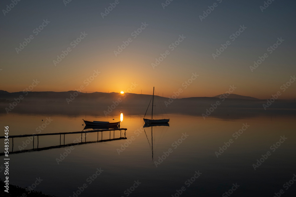 View of boats and pier on sunset sunrise or midday with reflection on water and sun light with cloudy sky View of boats and pier on sunset sunrise or midday with reflection on water and sun light with cloudy sky