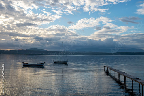 View of boats and pier on sunset sunrise or midday with reflection on water and sun light with cloudy sky