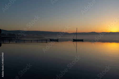 View of boats and pier on sunset sunrise or midday with reflection on water and sun light with cloudy sky