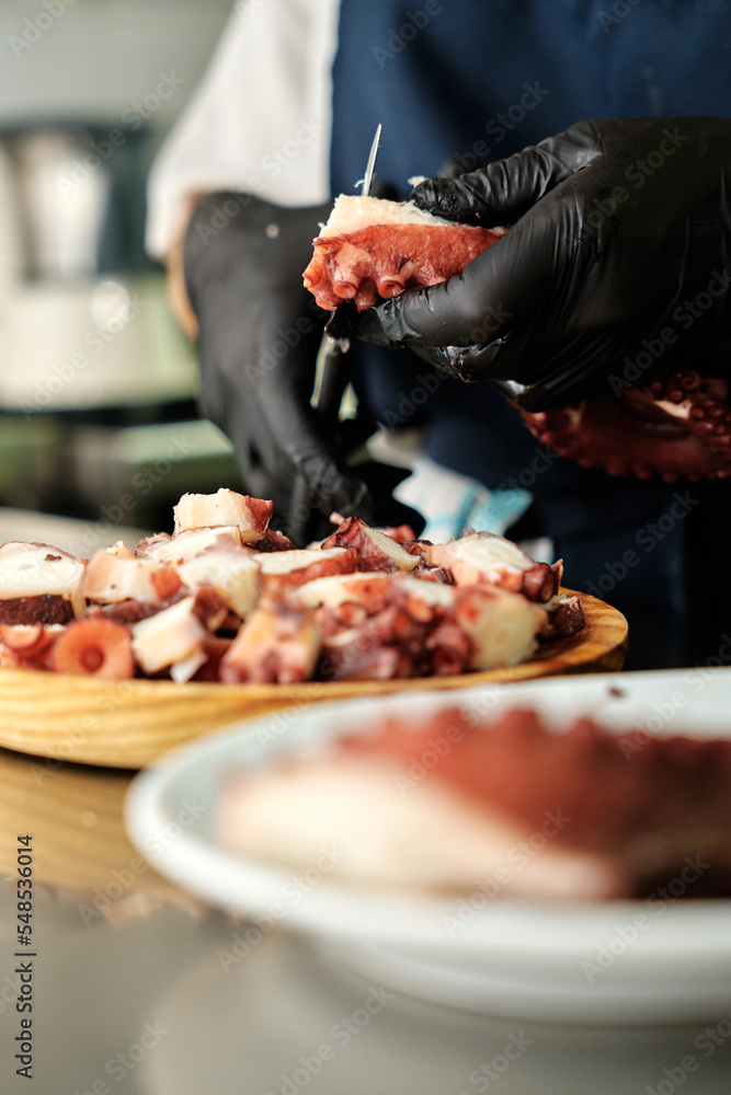 Chef cutting boiled octopus in a wooden round plate, no faces shown, close up look, vertical image