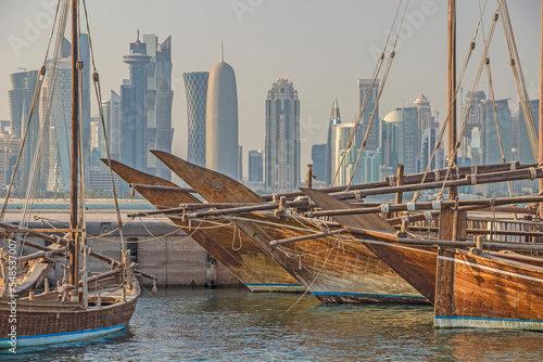 Qatar - Doha - Traditional wooden dhow boats moored at Dhow harbor in contrast with West Bay skyscrapers skyline on background photo
