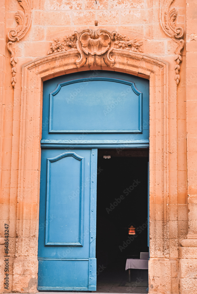 front view, medium distance of an entrance, with  to a pair of blue, wood doors, one open to a 1300's century, chapel, of limestone