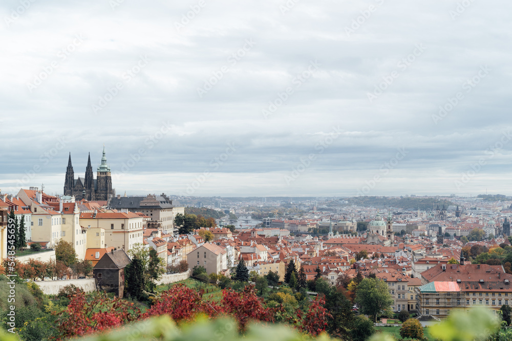 View of Prague castle and orange roofs from a hill colored with red foliage