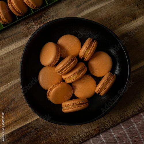 Top view of a bowl of orange-colored French macarons in a black bowl