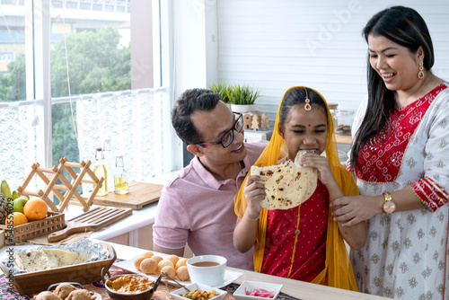Indian family with their dinner at modern kitchen at home  father mother and daughter having meal together  daughter in traditional dress tasting Indian naan bread  selective focus