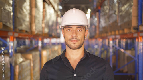 Portrait of middle east worker working in large warehouse retail store industry. Rack of stock storage. Interior of cargo in ecommerce and logistic concept. Depot. People lifestyle. Shipment service. © tampatra