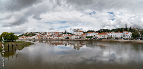 Landscape of Alcácer do Sal, Portugal on a dramatic, cloudy, day with buildings reflected in water. © Wormsmeat