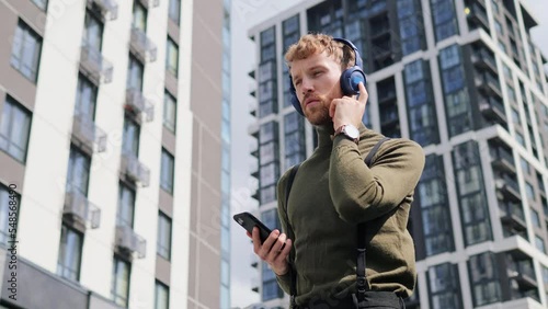 Wallpaper Mural Cheerful fashion guy wearing headphones standing outdoors dancing using smartphone music new app in modern city on summer day. Handsome man having fun, rest on urban street. People and music concept. Torontodigital.ca