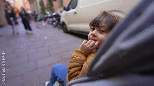 One little boy seated in stroller visiting city. Child doing tourism strolling in walkable street photo