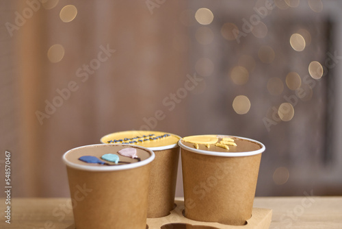 three homemade mini chocolate cake to go in coffee cup with cream drawing on a table, new confectionery trend concept. Paper cups with cakey are in a box. fashionable dessert. Horizontal, copy space