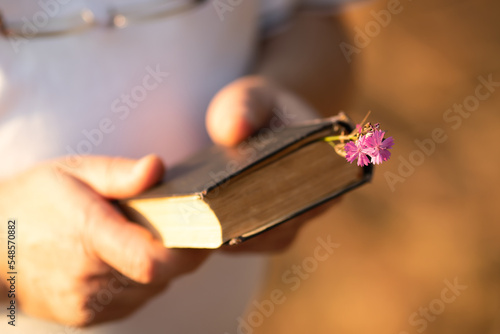 A caucasian man holds an old book in his hand on a bright sunny day. Close-up with a blurred background.