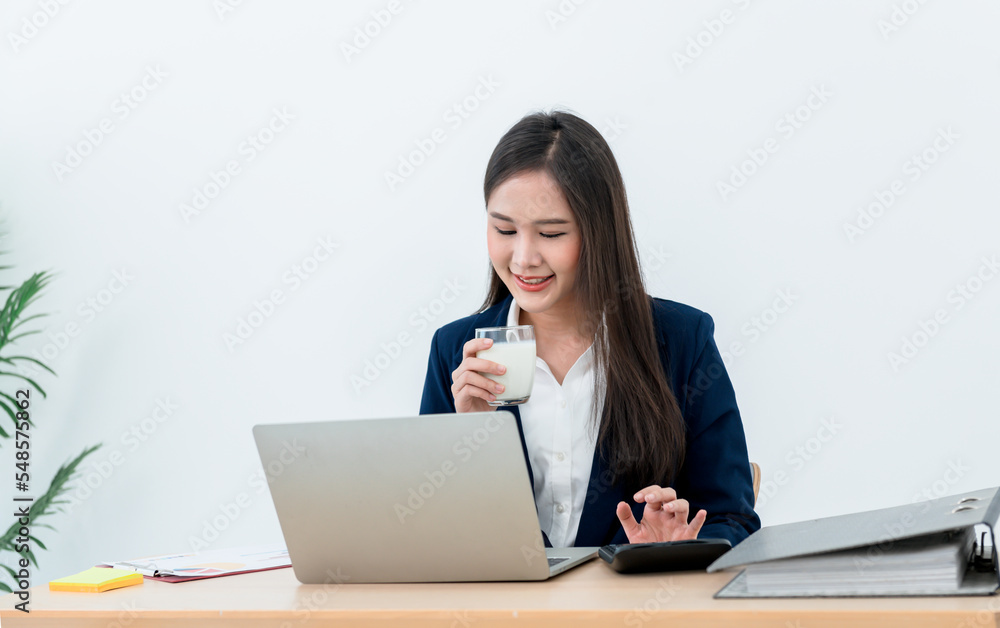 Asian businesswomen attractive and young drinking a milk in glass while working on the table because of urgent work. to business and food concept. Asian businesswomen attractive and young drinking a milk in glass while working on the table because of urgent work. to business and food concept.