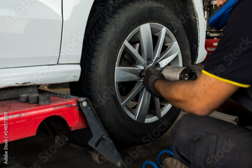 Auto mechanic man with electric screwdriver changing tire outside. Car service. Tire installation concept.