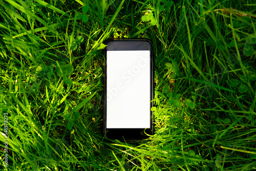 Mock up of a mobile phone with a empty space for text on the screen (touchscreen), on high grass, in the outdoor, in the shade, from a short distance, without anyone