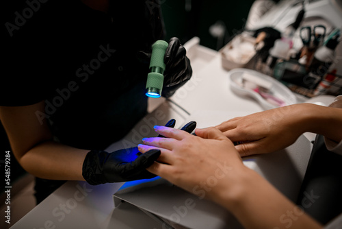 Close-up view of female hands use ultraviolet lamp for curing top cover of nail polish.