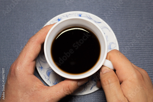 A man grabbing a cup of tea from a small saucer on a gray-blue cloth.