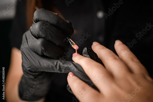 Master in gloves paints client nails with gel polish in the beauty salon.