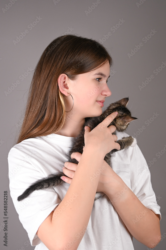 Teengirl holding a baby cat on gray background. Portrait of young girl with kitten. Kids and pets Teengirl holding a baby cat on gray background. Portrait of young girl with kitten. Kids and pets