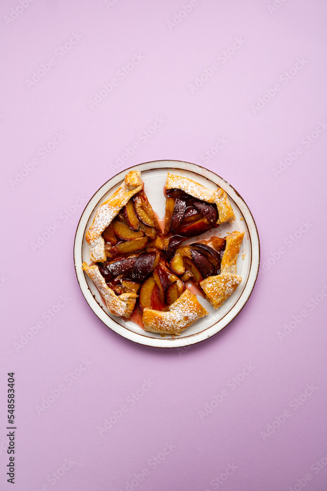 Overhead view of tasty sliced plum pie food on plate purple surface Overhead view of tasty sliced plum pie food on plate purple surface