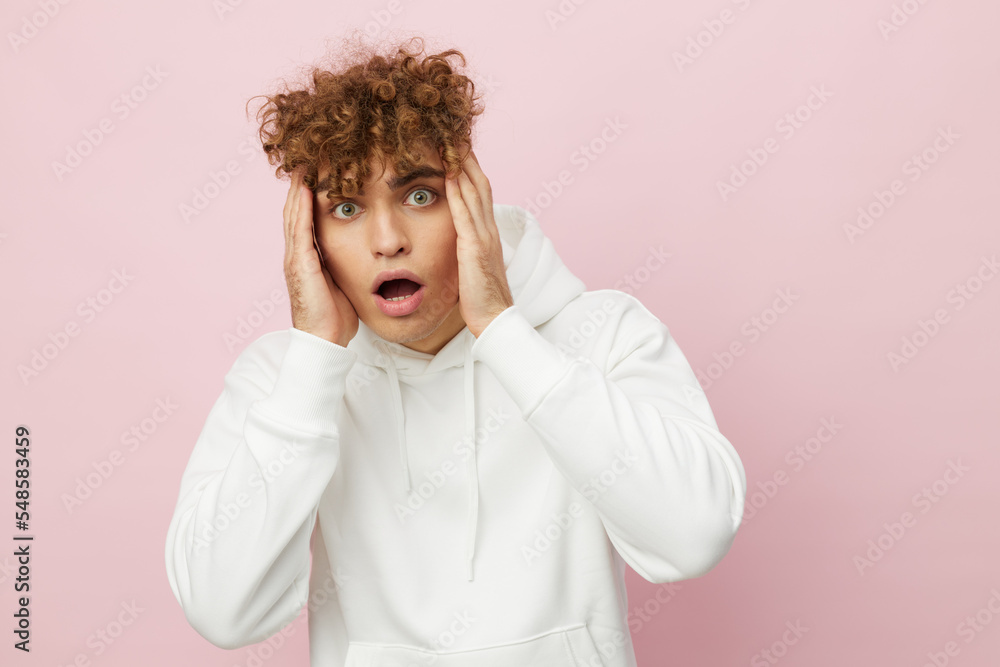 a funny, shocked man stands on a pink background in a white hoodie and looks at the camera with his mouth wide open in surprise, holding his hands near his face a funny, shocked man stands on a pink background in a white hoodie and looks at the camera with his mouth wide open in surprise, holding his hands near his face