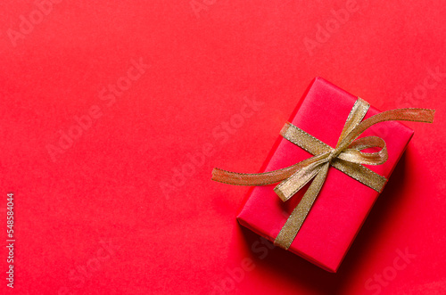 A red present with a golden ribbon on red background. Copy space. 