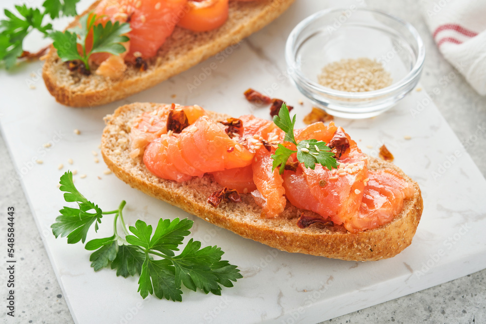 Sandwiches with salted salmon. Open sandwiches from cereal or whole grain rye bread with salted salmon, sesame seeds and dried tomato on white marble stand. Seafood. Healthy food. Scandinavian cuisine Sandwiches with salted salmon. Open sandwiches from cereal or whole grain rye bread with salted salmon, sesame seeds and dried tomato on white marble stand. Seafood. Healthy food. Scandinavian cuisine