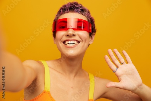 Woman wearing unusual millennial glasses taking selfies in sportswear against an orange studio background, free space